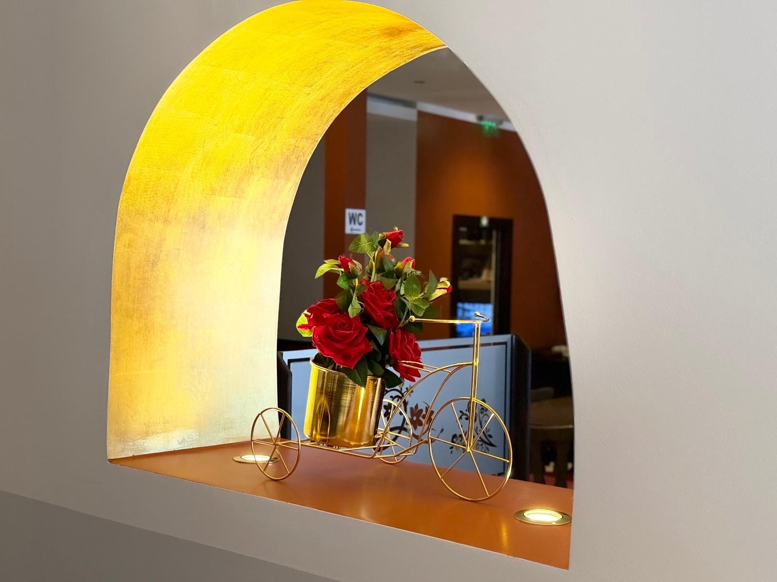 Dekoratives goldenes Deko-Fahrrad mit roten Rosen in einer Blattgold-Wandnische