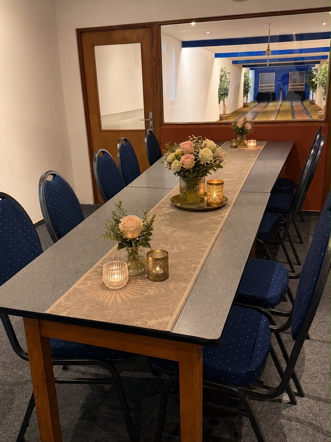Festlich eingedeckte Tafel mit Rosen und Kerzen und Blick durch die Scheibe auf die Kegelbahn